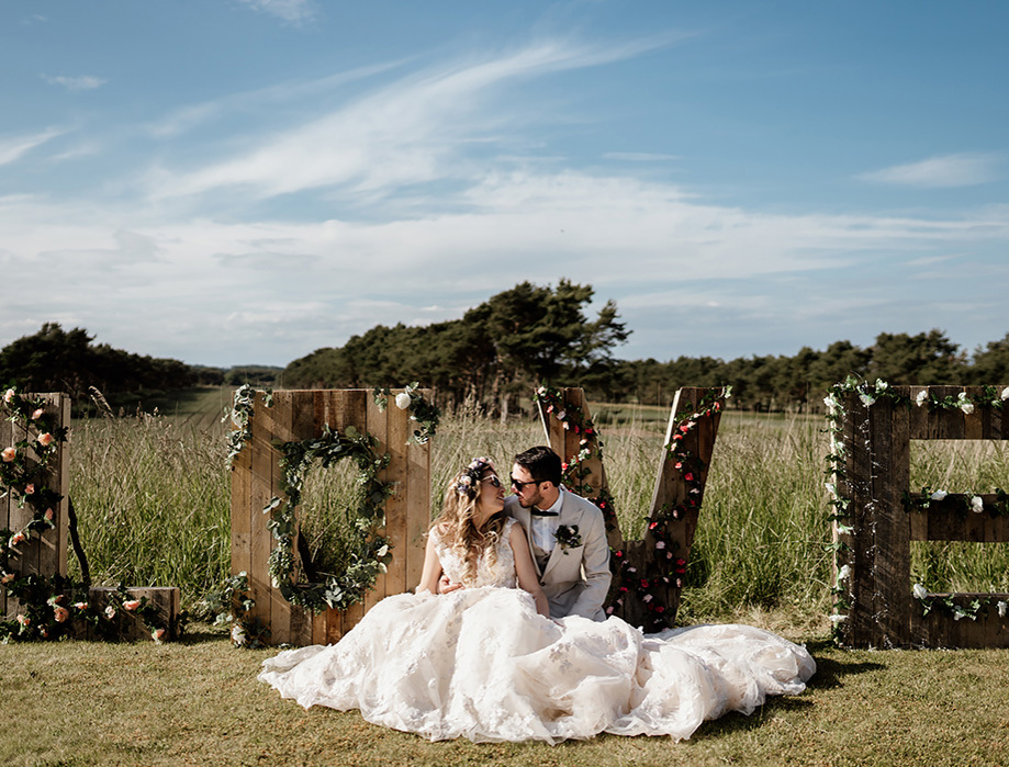 Bride and groom sit in front of floral decorated wooden letters spelling "Love"